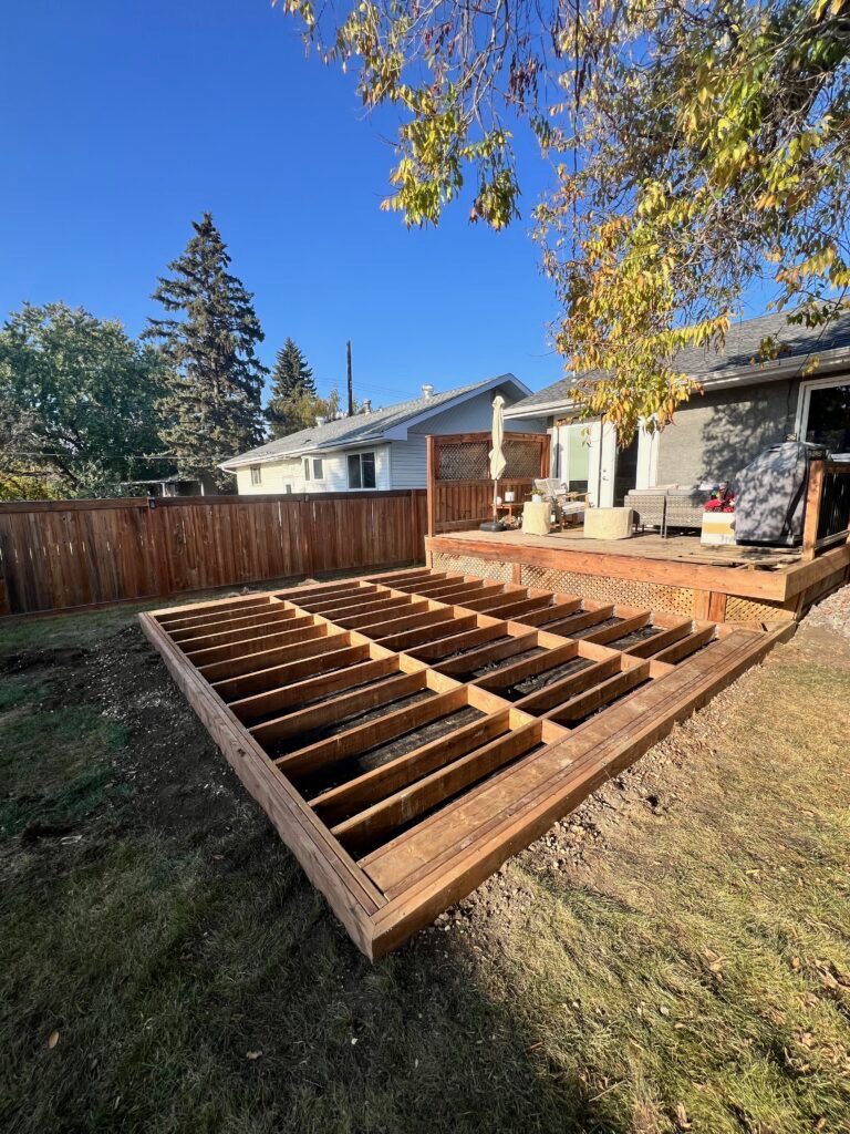 New ground-level deck frame with joists set beside an existing backyard deck